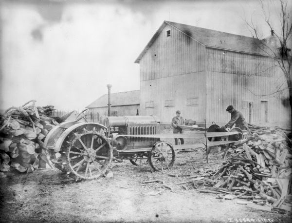Two man are using a McCormick-Deering tractor to belt-drive a saw to cut wood.