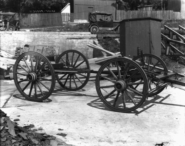 Wagon parts outdoors. Automobiles are parked in the background.