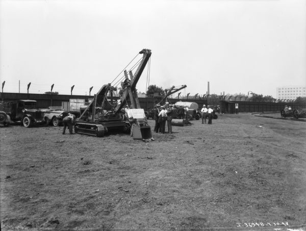 Men looking at demonstration of IH implements set up outdoors, probably in a factory yard. Long wood fences are in the background.