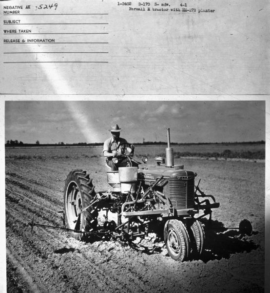 Three-quarter view from front right of  man driving a Farmall H tractor in a field. Information with photograph reads: "Farmall H tractor with HM-278 planter."