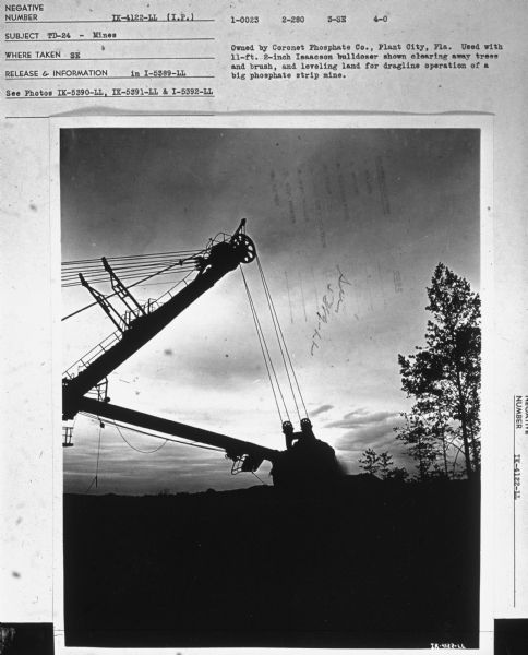 A bulldozer removing trees is silhouetted against the sky. Subject: "TD-24 — Mines." Where Taken: "SE." Information with photograph reads: "Owned by Coronet Phosphate Co., Plant City, Fla. Used with 11-ft. 2-inch Isaacson bulldozer shown clearing away trees and brush, and leveling land for dragline operation of a big phosphate strip mine."