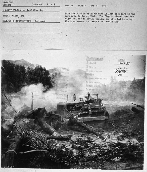 Elevated view of a  man using a TD-18A to cover up a fire. Subject: "TD-18A — Land Clearing." Where Taken: "MtS." Information with photograph reads: "This TD-18 is covering up what is left of a fire in the park area in Ogden, Utah. The fire continued thru the night and the following morning the city had to cover the tree stumps that were still smoldering."