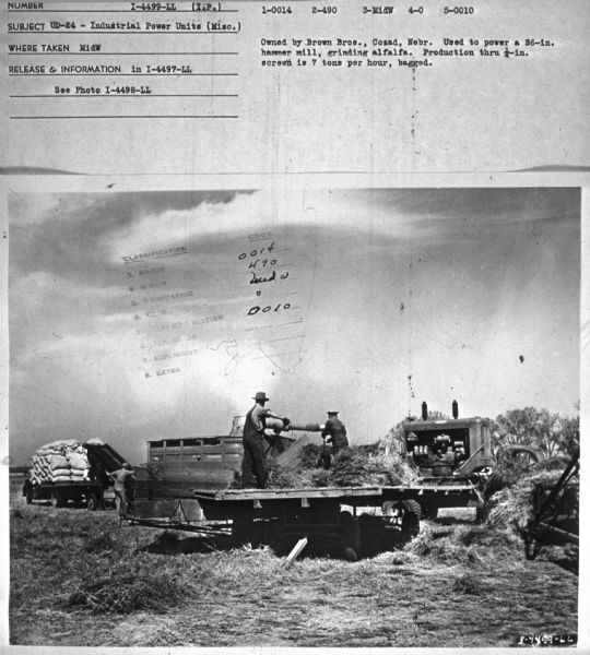 Men are standing on a trailer working with alfalfa. The UD-24 is on the back of a truck. Subject: "UD-24 — Industrial Power Units (Misc.)." Where Taken: "MidW." Information with photograph reads: "Owned by Brown Bros., Cozad, Nebr. Used to power a 36-in. hammer mill, grinding alfalfa. Production through 1/4-in. screen is 7 tons per hour, bagged."