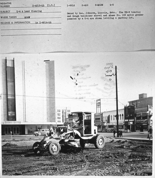 View towards a man clearing a parking lot. There is a large building in the background. Subject: "U4 & Land Clearing." Where Taken: "MidW." Information with photograph reads: "Owned by Geo. Johnson, Lincoln, Nebr. The TD-9 tractor and Hough bulldozer shovel and Adams No. 102 motor grader powered by a U-4 are shown leveling a parking lot."