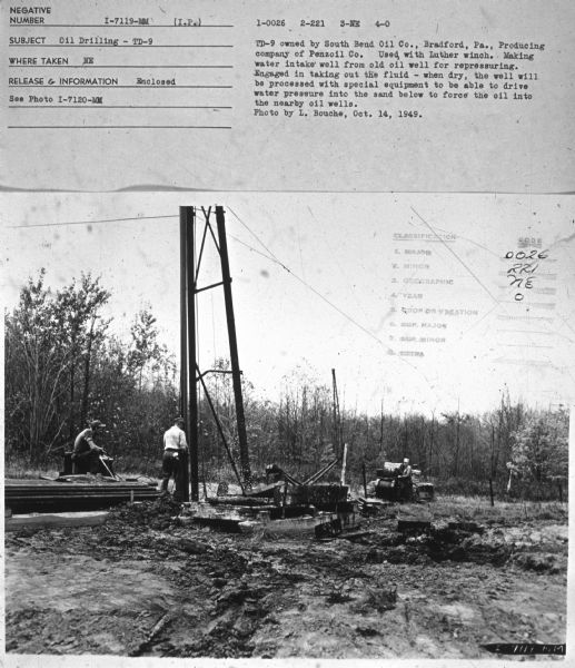 Three men are working outdoors. Subject: "Oil Drilling — TD-9." Where Taken: "NE." Information with photograph reads: "TD-9 owned by South Bend Oil Co., Bradford, Pa., Producing company of Penzoil Co. Used with Luther winch. Making water intake well from old oil well for repressuring. Engaged in taking out the fluid — when dry, the well will be processed with special equipment to be able to drive water pressure into the sand below to force the oil into the nearby oil wells. Photo by L. Bouche, Oct. 14, 1949."	