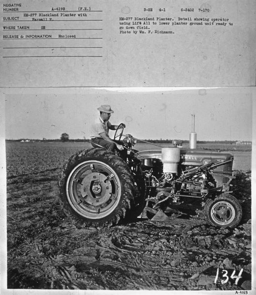 Right side view of a man sitting on a Farmall H tractor in a field. Subject: "HM-277 Blackland Planter with Farmall H." Where Taken: "SE." Information with photograph reads: "HM-277 Blackland Planter. Detail showing operator using Life-All to lower planter ground unit ready to go down field. Photo by Wm. F. Eichmann."