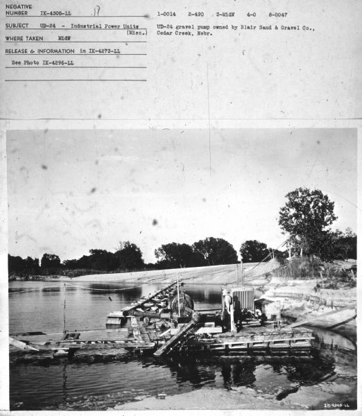 View towards a man standing on a pier with a UD-24. Subject: "UD-24 — Industrial Power Units." Where Taken: "MidW." Information with photograph reads: "UD-24 gravel pump owned by Blair Sand & Gravel Co., Cedar Creek, Nebr."