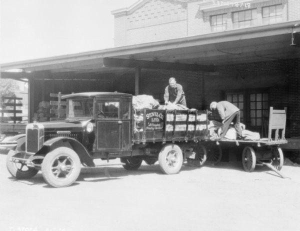 Two men are standing on a loading dock. A Stovel Co. Ltd. truck, "A Complete Printing Service" is backed up to the dock. 