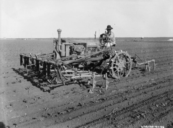 A man is using a Farmall tractor with a cultivator in a field.