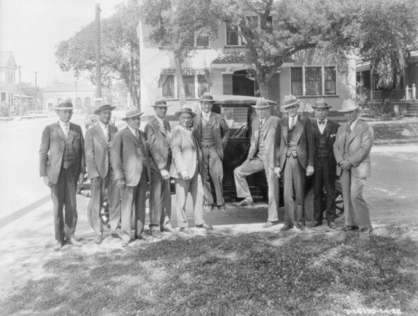 Outdoor group portrait of businessmen posing on the sidewalk in front of a truck parked along the curb.