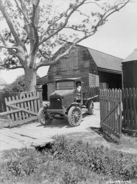 View towards a man driving a farm truck through a gate on a farm. In the background is a barn.