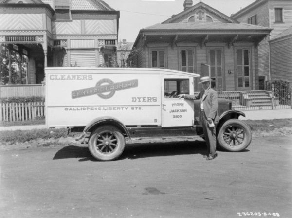 View across street towards a man sitting in the driver's seat of a truck parked in a neighborhood. Another man is standing near the open window of the passenger side of the truck. The sign on the truck reads: "Central Laundry, Cleaners, Dyers."