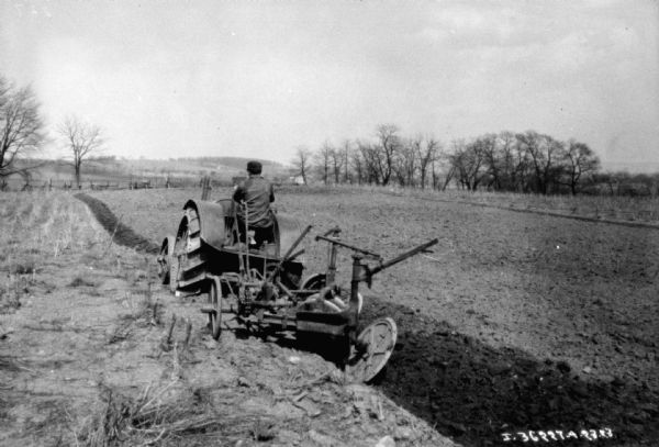 Rear view of a man using a tractor to pull a plow in a field.