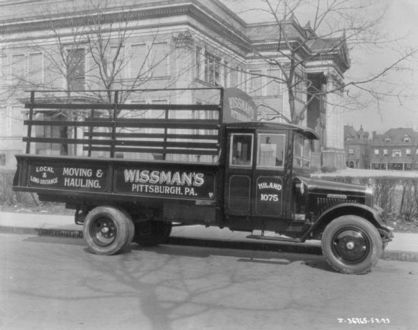 View across street towards the passenger side of a delivery truck parked along a curb. The sign painted on the truck reads: "Wissman's, Moving & Hauling."