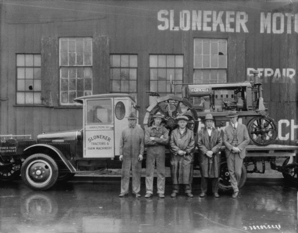 View of a group of people posing outdoors in the rain in front of Sloneker Motor & Implement Co. Inc.