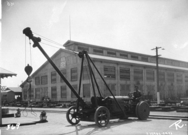 A man is using an industrial tractor to a crane attached to the front while working at a warehouse.