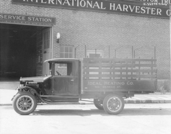 View across street towards a delivery truck parked in front of a brick building with a sign that reads: "International Harvester Co." The sign on the truck reads: "Ideal Heating Co."