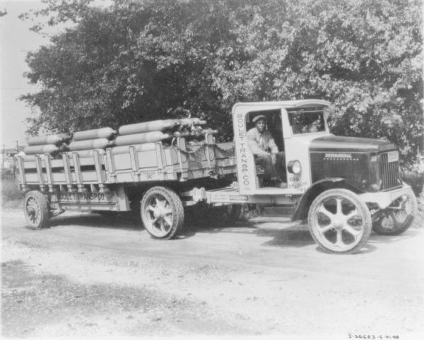 View towards a man sitting in the passenger seat of a delivery truck pulling a trailer. The sign painted on the truck reads: "Boulet Transp. Co. Inc."