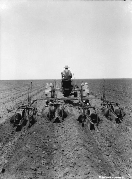 Rear view of a man driving a tractor pulling a planter in a field.