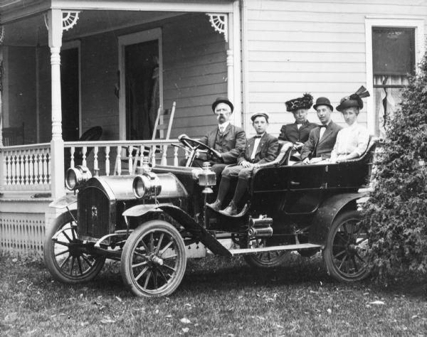 Two men, two women, and a boy are posing sitting in an automobile parked in the yard next to a frame house. Probably Eugene J. Greenlee and son Eugene in the front, and Mrs. Greenlee, Byron Greenlee, and Irma Greenlee Reichenbach in the back seat. They are seated in "The Silent Northern."