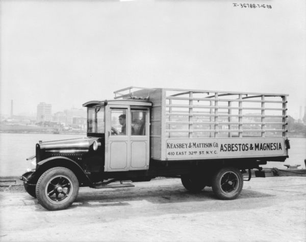 View towards driver's side of a delivery truck. There is water in the background, and buildings are on the far shoreline. The sign on the side of the truck reads: "Keasbey & Mattison Co. Asbestos & Magnesia."