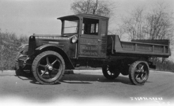 View towards the driver's side of a delivery truck parked along a curb. The sign painted on the side reads: "General Hauling."