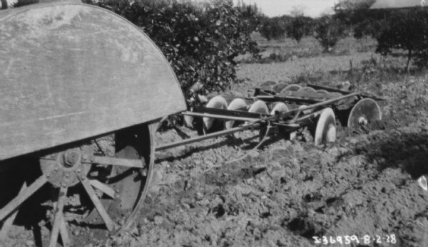 View of back left side of tractor pulling a disk harrow in a field or orchard.