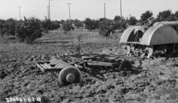 View of back side of tractor pulling a disk harrow in a field or orchard.