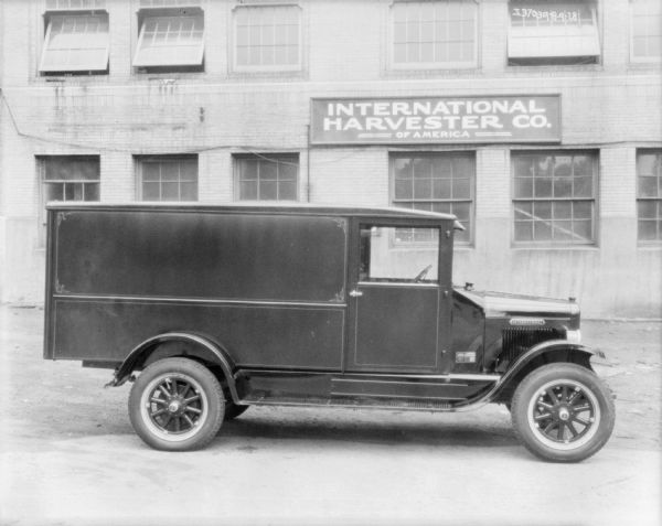 View towards the passenger side of a truck parked in front of a brick building. The sign on the building behind the truck reads: "International Harvester of America."