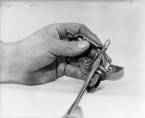 Close-up of a person's hand making an adjustment on a part with a screwdriver.