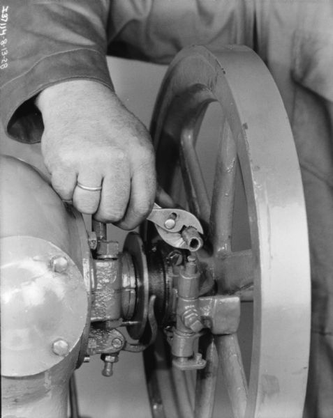 Close-up of a man's hands making adjustments making adjustments on a 1 1/2 H.P. engine.