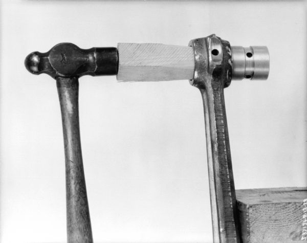 Close-up of a hammer resting on a block of wood in a metal part for a McCormick-Deering 1 1/2 H.P. engine.
