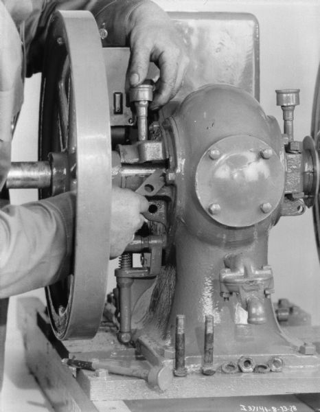 View of a man (head out of frame) using tools to maintain a 1 1/2 H.P. engine.