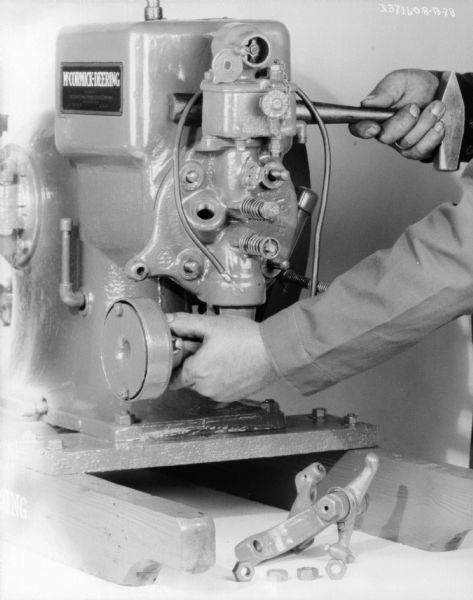 Close-up of a man (head out of frame) making adjustments on a McCormick-Deering 1 1/2 H.P. engine.