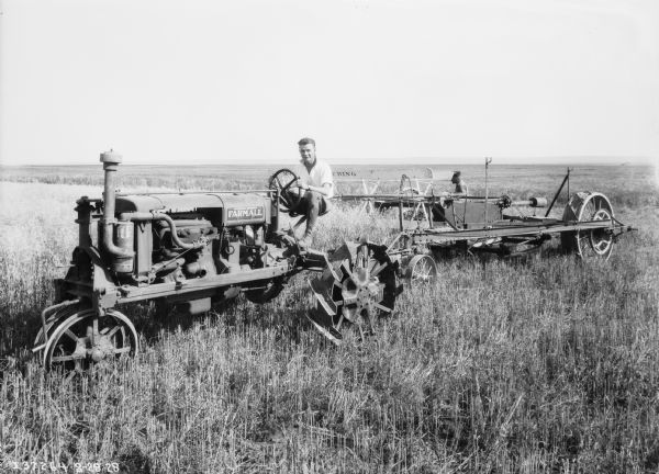 Left side view of a man driving a Farmall tractor pulling push binders in a field. Another man is standing in the background behind the push binders.