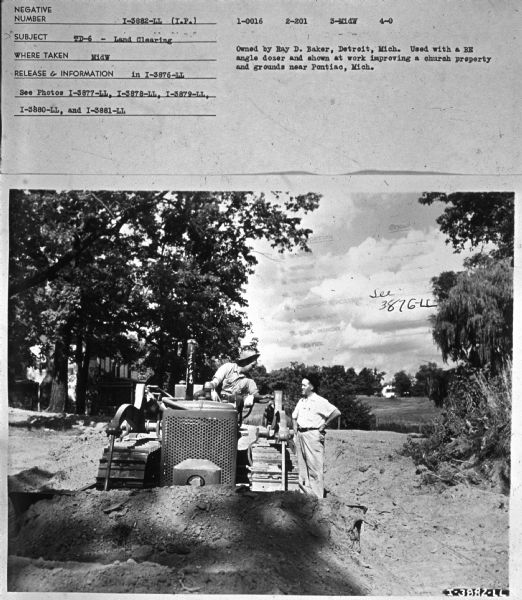 View of a man sitting on a TD-6, and talking to a man standing on the right. Subject: "TD-6 — Land Clearing." Where Taken: "MidW." Information with photograph reads: "Owned by Bay D. Baker, Detroit, Mich. Used with a RE angle dozer and shown at work improving a church property and grounds near Pontiac, Mich." 