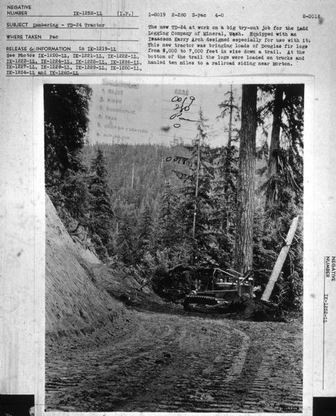 View down road towards a man using a TD-24 tractor. Mountains are in the background. Subject: "Lumbering — TD-24 Tractor." Where Taken: "Pac." Information with photograph reads: "The new TD-24 at work on a big try-out job for the Ladd Logging Co., of Mineral, Wash. Equipped with an Isaacson Karry arch designed especially for use with it. This new tractor was bringing loads of Douglas fir logs from 6,000 to 7,000 feet in size down a trail. At the bottom of the trail the logs were loaded on trucks and hauled ten miles to a railroad siding near Morton."