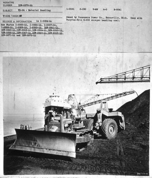 View towards a man driving a TD-24. In the background are cranes, and a ship at the shoreline. Subject: "TD-24 — Material Handling." Where Taken: "MW." Information with photograph reads: "Owned by Consumers Power Co., Essexville, Mich. Used with Bucyrus-Erie B-250 scraper handling coal."