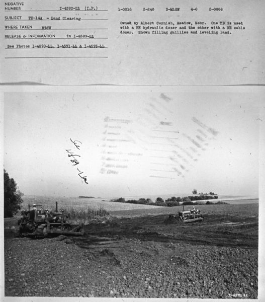 View of two men working filling gullies and leveling land. Subject: "TD-14A — Land Clearing." Where Taken: "MidW." Information with photograph reads: "Owned by Albert Cornish, Meadow, Nebr. One TD is used with a BE hydraulic dozer and the other with a BE cable dozer. Shown filling gullies and leveling land."	