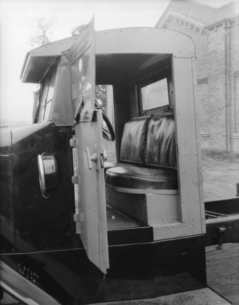 Close-up view through the open driver's side door into the cab of a truck. A brick building is in the background.