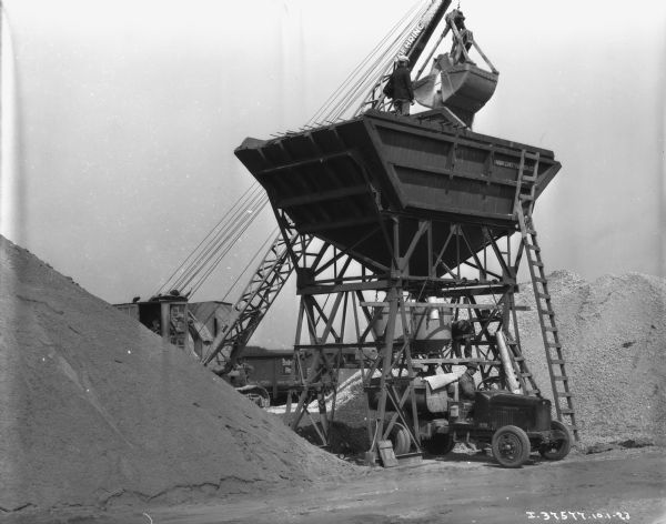 Men are working with a large chute and a crane to load trucks with coal.