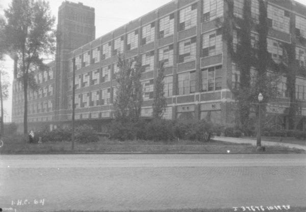 View across street towards a large building. People are walking on the opposite sidewalk on the far left.