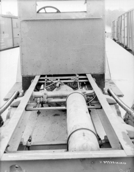 View from rear towards the cab of a truck, which appears to be on a railroad platform. The truck bed is exposed. Railroad cars are on the left and right.
