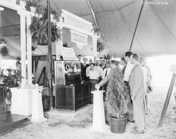 A group of people are standing around the IH exhibit. Signs read: "McCormick-Deering Ball-Bearing Cream Separators" and "McCormick-Deering Cream Separators are equipped with New Departure Ball-Bearings."