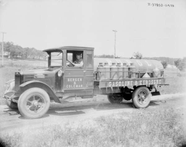 View towards a man sitting in the driver's seat of a gasoline delivery truck. The sign painted on the door reads: "Bergen & Coleman, Pupol Gasoline & Kerosene."