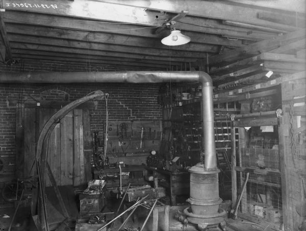 View of the interior of a repair shop. A wood burning stove is on the right, and tools are hanging on a board on the wall in the background.