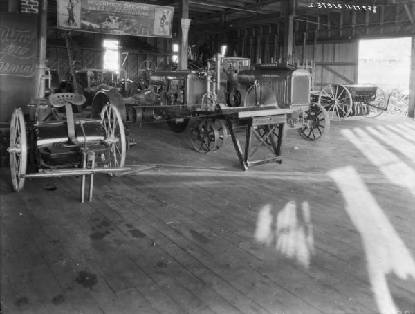 Interior view of agricultural machinery, tractors, etc., at a dealership. On the right is an open garage door. Hanging from the ceiling is a banner that reads: "McCormick-Deering Ball-Bearing Cream Separators."