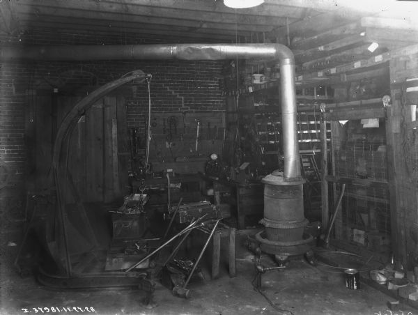 Interior view of repair shop at implement store. A wood burning stove is in the center, and tools are hanging on a board on the wall on the left. Parts are on shelves in the background.