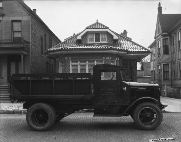 View across cobblestone street towards a truck parked in front of a house. The sign painted on the passenger side door reads: "Nick Schmit."