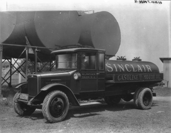 View towards driver's side of a Sinclair gas truck, parked in front of gas tanks. The sign painted on the driver's side door reads: "W.L. Matlack, Salem, N.J."